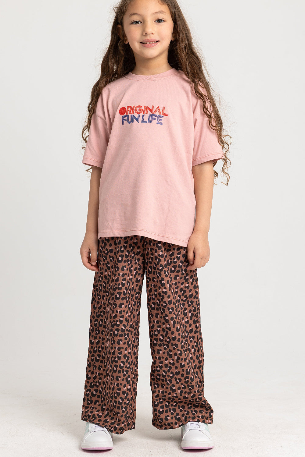 Young girl wearing a pink t-shirt with text and leopard print pants on a white background