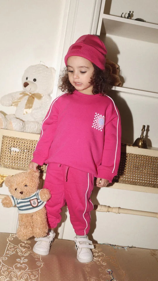 toddler in a fuchsia tracksuit with a teddy